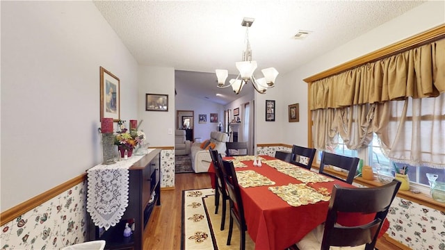 dining space featuring visible vents, a chandelier, lofted ceiling, light wood-style floors, and a textured ceiling