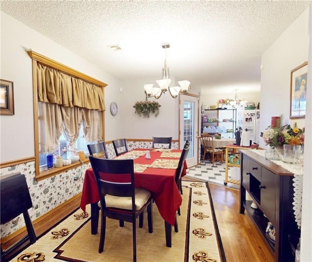 dining space featuring wallpapered walls, a textured ceiling, an inviting chandelier, and light wood finished floors