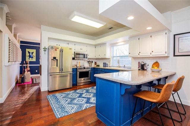 kitchen with tasteful backsplash, white cabinets, appliances with stainless steel finishes, and a peninsula