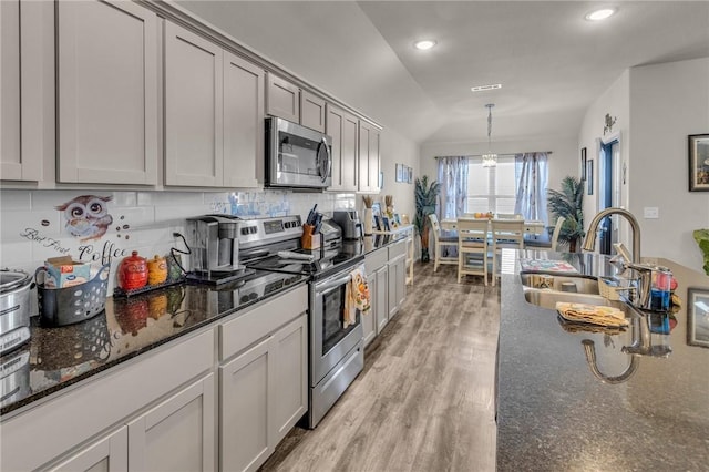 kitchen featuring backsplash, light wood-type flooring, vaulted ceiling, appliances with stainless steel finishes, and a sink