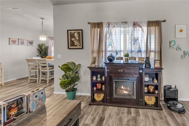 sitting room featuring visible vents, a warm lit fireplace, baseboards, and wood finished floors