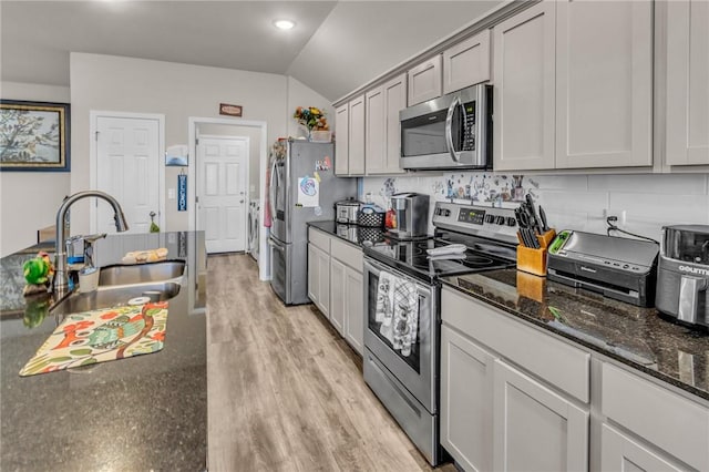 kitchen with light wood-type flooring, dark stone countertops, washer / dryer, stainless steel appliances, and a sink