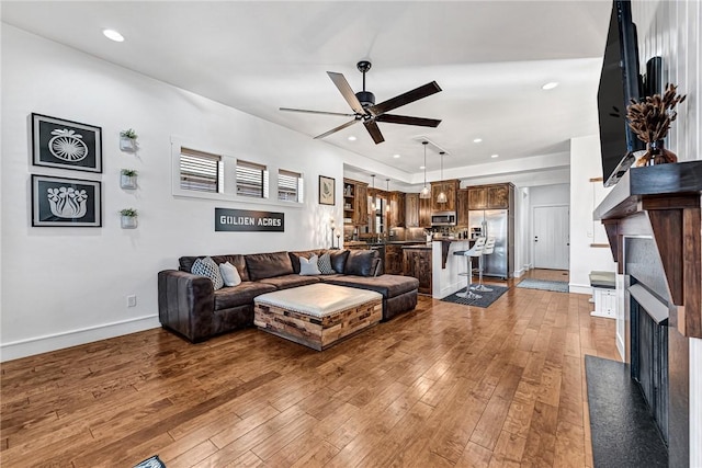 living area featuring baseboards, ceiling fan, a fireplace with flush hearth, recessed lighting, and light wood-style flooring