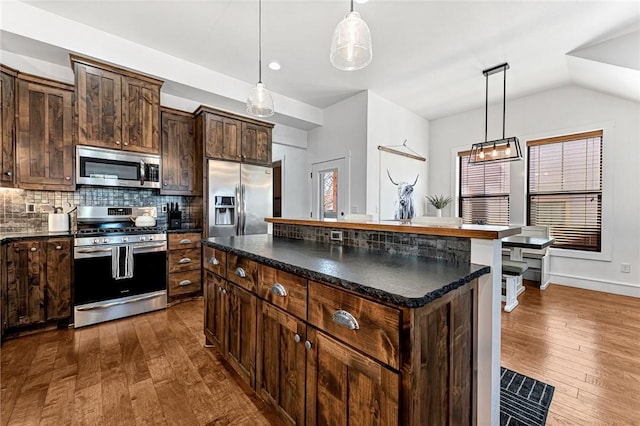 kitchen featuring dark countertops, dark brown cabinetry, decorative backsplash, stainless steel appliances, and dark wood-style flooring