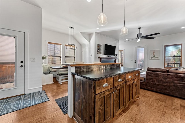 kitchen with light wood-type flooring, decorative light fixtures, dark countertops, open floor plan, and ceiling fan