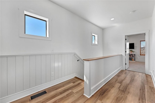 corridor featuring wood finished floors, an upstairs landing, visible vents, and a healthy amount of sunlight