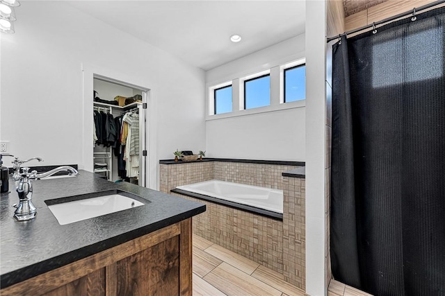 full bath with a spacious closet, curtained shower, a garden tub, and a sink