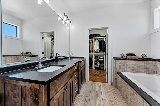 full bathroom with a bath, a spacious closet, double vanity, and a sink