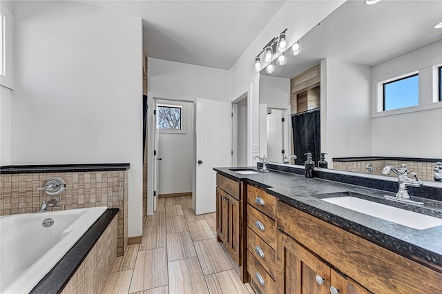 full bath with tiled bath, double vanity, baseboards, and a sink