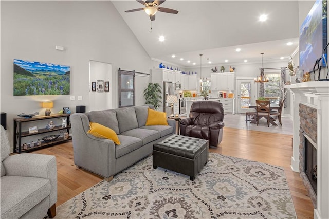 living area with a stone fireplace, a barn door, light wood-type flooring, and high vaulted ceiling