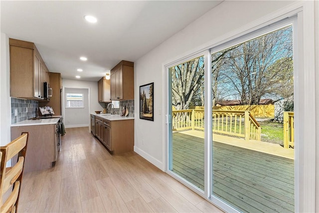 kitchen with a sink, backsplash, appliances with stainless steel finishes, light wood finished floors, and light countertops