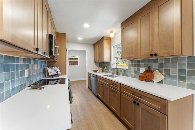 kitchen featuring backsplash, light countertops, light wood-style flooring, appliances with stainless steel finishes, and a sink