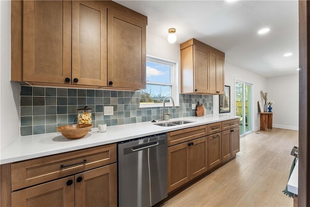 kitchen with backsplash, dishwasher, light countertops, light wood-style flooring, and a sink