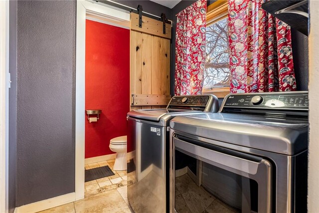 clothes washing area with washer and dryer, a barn door, light tile patterned floors, baseboards, and laundry area