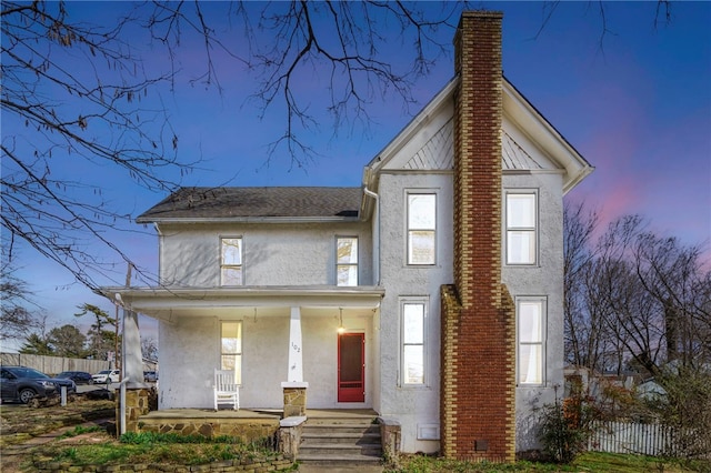 view of front of house featuring stucco siding, a porch, a chimney, and fence