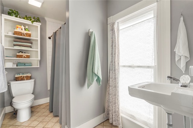 bathroom featuring baseboards, toilet, a shower with shower curtain, tile patterned floors, and a sink