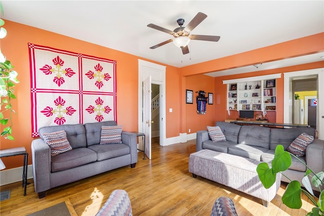 living area with a ceiling fan, baseboards, built in features, and wood finished floors