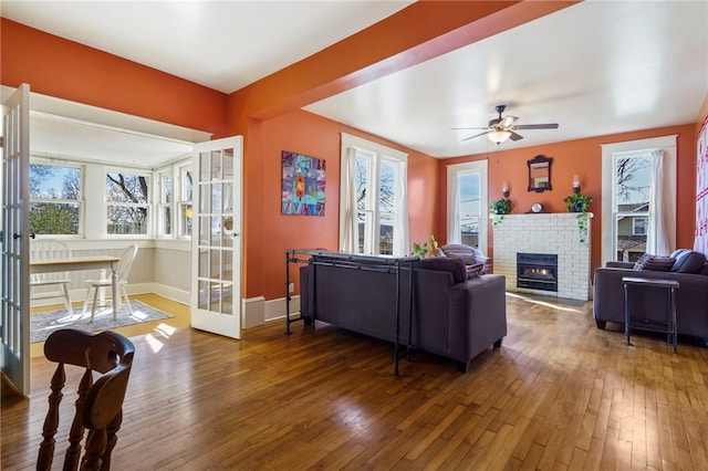 living room with hardwood / wood-style floors, a ceiling fan, baseboards, a fireplace, and french doors