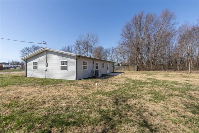 rear view of property featuring central AC unit, a lawn, and fence