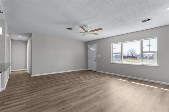 unfurnished living room with visible vents, baseboards, a textured ceiling, and wood finished floors