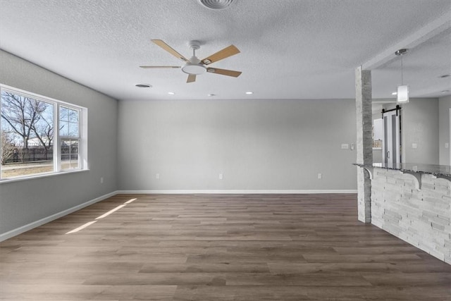 unfurnished living room featuring wood finished floors, baseboards, ceiling fan, a textured ceiling, and a barn door