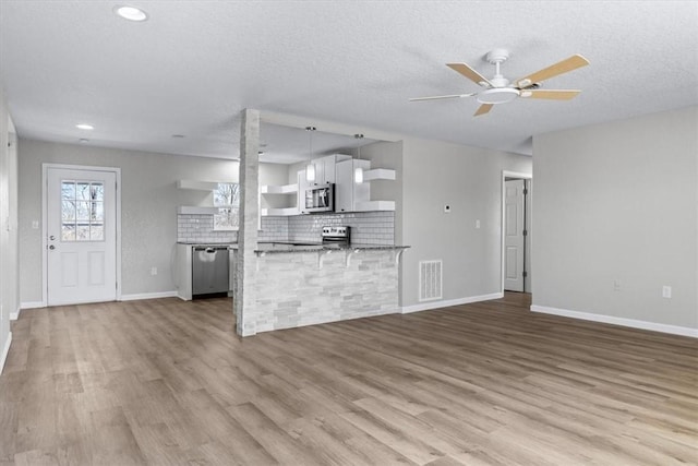 unfurnished living room featuring wood finished floors, visible vents, baseboards, ceiling fan, and a textured ceiling