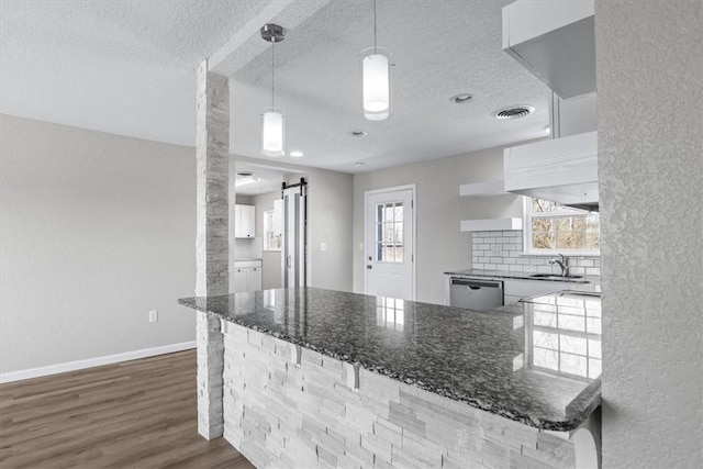 kitchen with tasteful backsplash, dark wood-type flooring, a barn door, a peninsula, and stainless steel dishwasher