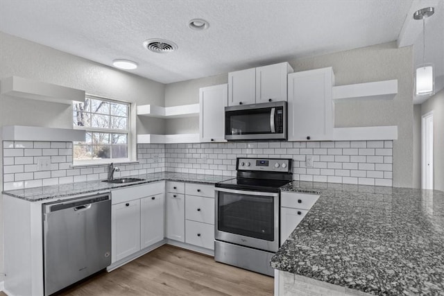 kitchen with visible vents, open shelves, dark stone countertops, a sink, and stainless steel appliances