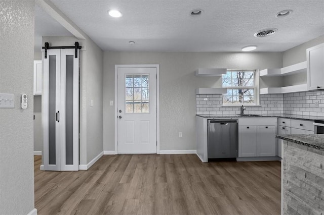 kitchen with visible vents, open shelves, decorative backsplash, dishwasher, and a barn door