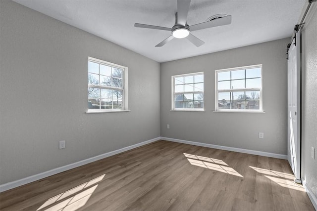 unfurnished bedroom with a ceiling fan, a barn door, wood finished floors, and baseboards