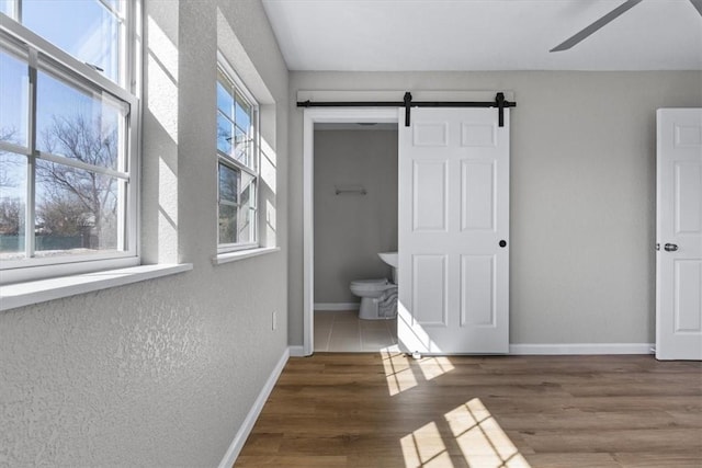 interior space with multiple windows, baseboards, a barn door, and wood finished floors