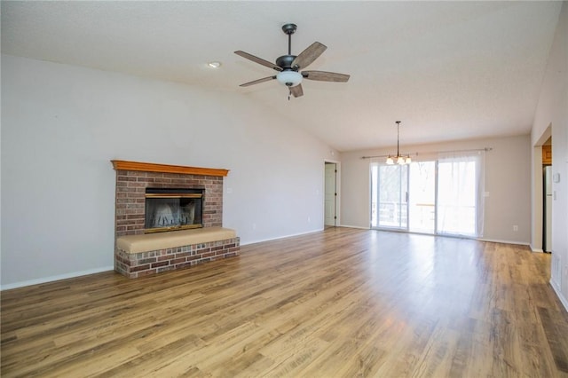 unfurnished living room featuring lofted ceiling, a brick fireplace, wood finished floors, and ceiling fan with notable chandelier