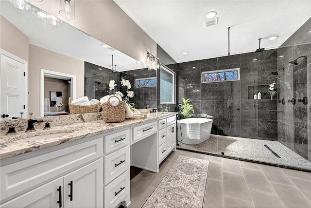 bathroom featuring visible vents, double vanity, tiled shower, a freestanding tub, and a sink