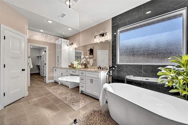 full bathroom featuring a spacious closet, visible vents, double vanity, recessed lighting, and a soaking tub