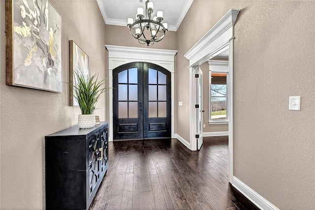 foyer entrance featuring a notable chandelier, french doors, crown molding, baseboards, and dark wood-style flooring