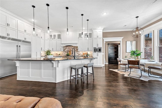 kitchen featuring tasteful backsplash, crown molding, built in appliances, a breakfast bar area, and dark wood-style flooring