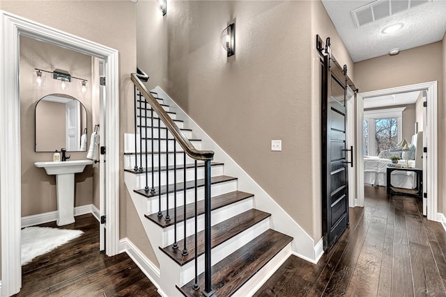 staircase with baseboards, visible vents, hardwood / wood-style flooring, a textured ceiling, and a barn door