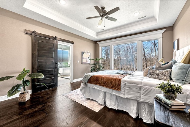 bedroom featuring a barn door, visible vents, a textured ceiling, and a tray ceiling