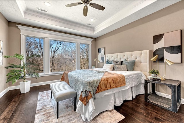 bedroom featuring visible vents, ornamental molding, hardwood / wood-style flooring, a tray ceiling, and a textured ceiling