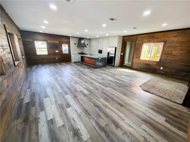 unfurnished living room with wooden walls, recessed lighting, wood finished floors, and visible vents