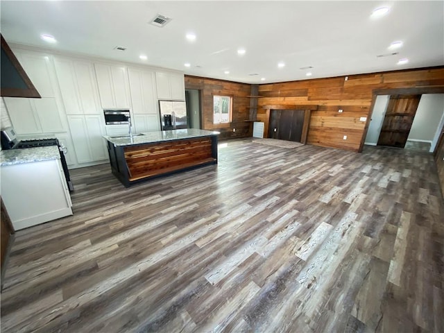 kitchen featuring a center island with sink, visible vents, stainless steel fridge with ice dispenser, dark wood-style flooring, and white cabinetry