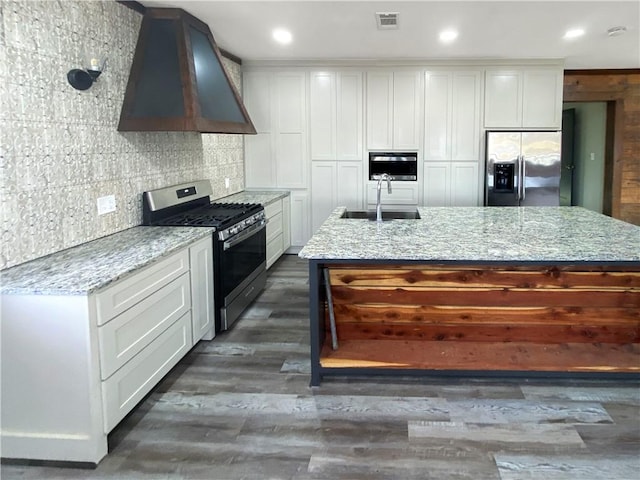 kitchen with a sink, light stone counters, white cabinetry, stainless steel appliances, and custom exhaust hood