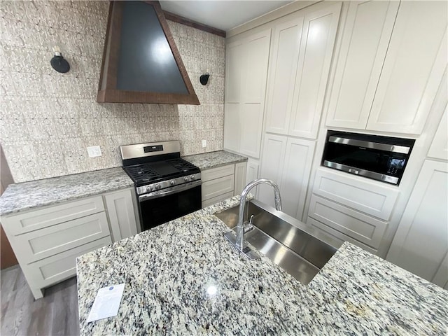 kitchen with light stone counters, decorative backsplash, stainless steel appliances, wall chimney exhaust hood, and a sink