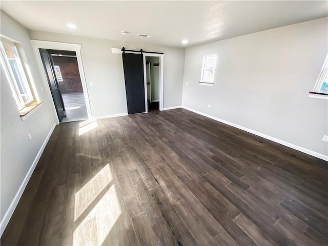 unfurnished bedroom featuring visible vents, baseboards, dark wood finished floors, recessed lighting, and a barn door