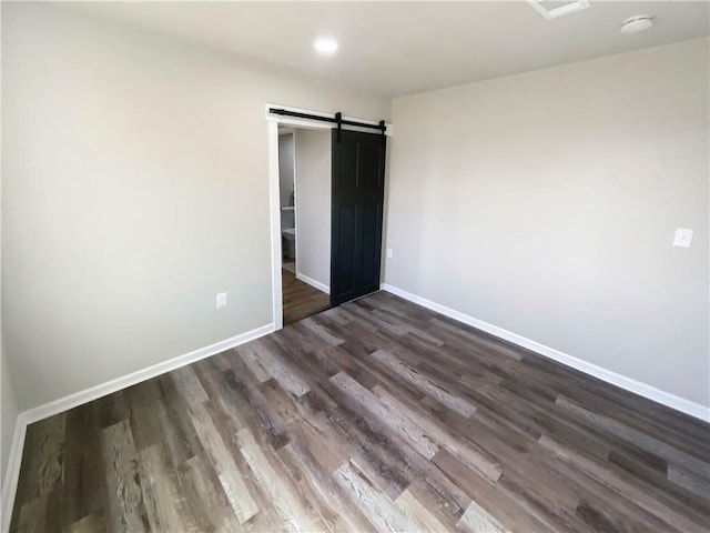 unfurnished bedroom with dark wood finished floors, a barn door, and baseboards