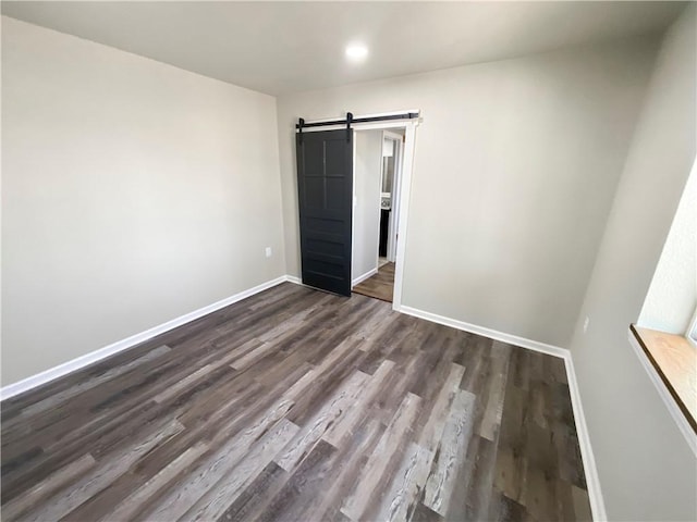 unfurnished bedroom with dark wood-style floors, baseboards, and a barn door