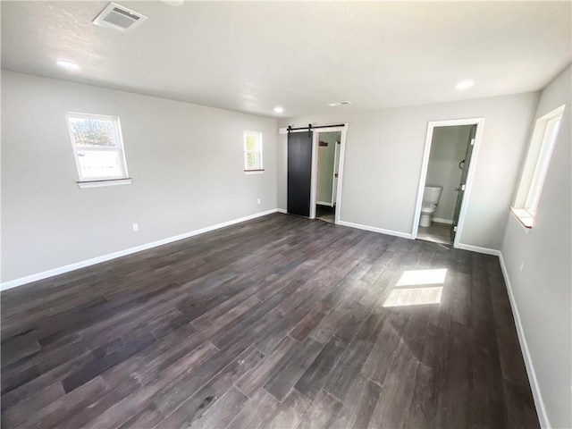 unfurnished bedroom with a barn door, baseboards, visible vents, and dark wood-style floors