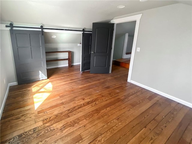 unfurnished bedroom with a barn door, wood finished floors, and baseboards