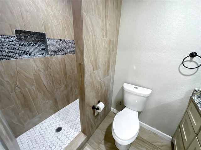 bathroom with vanity, baseboards, a tile shower, toilet, and a textured wall