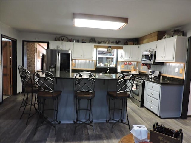 kitchen with dark countertops, appliances with stainless steel finishes, wood finished floors, and white cabinetry